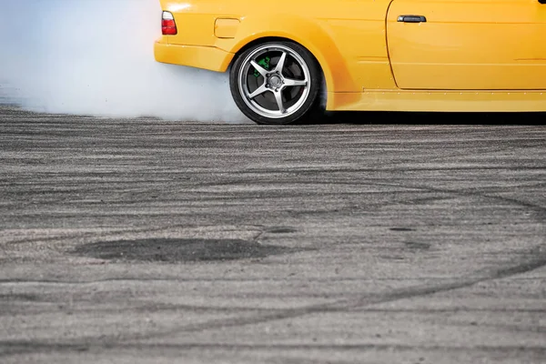 stock image closeup side view of yellow sport car drifting on gray speed tarmac track with white smoke coming out of the back tire wheel with copy space available