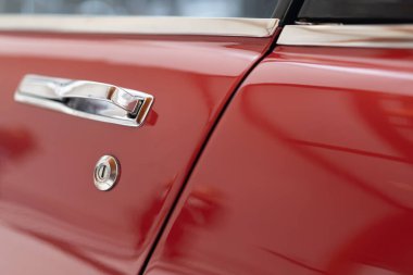 Eski bir araba kapı kolunun yakın çekimi. Kırmızı bir vücutta cilalanmış krom var. Eski zarafeti vurguluyor.