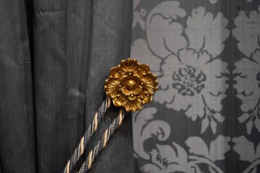 Dekoratif altın kravat, kapalı bir yerde çiçekli gri bir perde ve zarif iç dekorasyon için yumuşak bir ışık tutuyor.