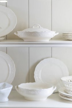 Klasik ve zarif mutfak dekorasyonu için raflara yerleştirilmiş beyaz porselen tabaklar ve servis malzemeleri.