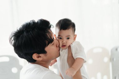 Babalığın mutluluğu işte. Evinin penceresinin yanında duran sevimli bebeği olan genç Asyalı baba. Sevgi dolu baba, küçük çocukla vakit geçiriyor. Babalar Günü konsepti.