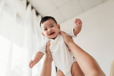 Asyalı sevimli bebek iyi bir ruh hali içinde, ebeveynleriyle oynamaktan zevk alıyor. Bir ebeveyn kucağına küçük bir bebek alıp oynamaya başlıyor..