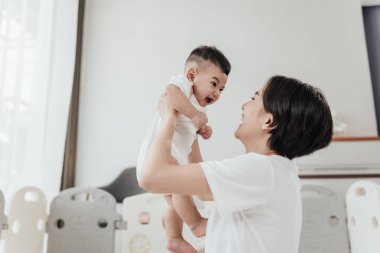 Sevimli Asyalı bebek annesiyle oynarken iyi eğlenceler. Asyalı anne yeni doğmuş bebeği kaldırıyor ve oynuyor mutlu Asyalı aile sağlık hizmetleri anneler günü konsepti. Seçici odak.