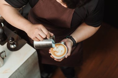 Manzaralı, Barista sütlü köpüğü sütlü kahve yapmaya koyuyor. Kahve dükkanında çalışan genç bir barista. Latte sanat menüsü kahvesi, Espresso, kahve menüsü yapma konsepti. Seçici odak.