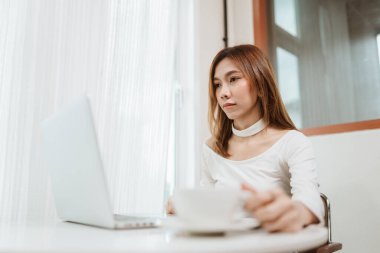 Kahve dükkanında bilgisayarla çalışan bir iş kadını. Asyalı kadın sabahları kahveyle dinleniyor..