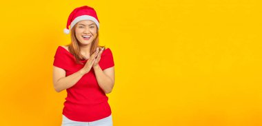 Gülümseyen genç kadın, sarı arka plan konferansında Noel şapkası takıp alkışlıyor.