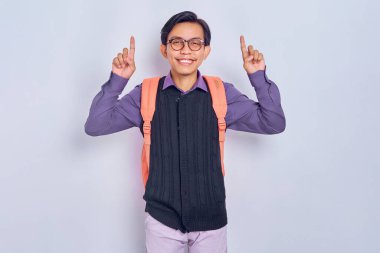 Sırt çantalı, kolejden neşeli, genç Asyalı erkek öğrenci gri arka planda parmak izine sahip bir şeyi işaret ediyor. Lise üniversite konsepti eğitimi