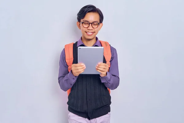 stock image Smiling young Asian male student from a college in casual clothes with a backpack using a digital tablet isolated on grey background. Education in high school university college concept