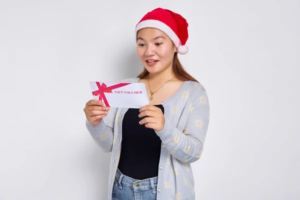 Surprised young Asian woman 20s in hat Christmas receives a gift certificate coupon voucher card isolated on white studio background. Merry Christmas Concept