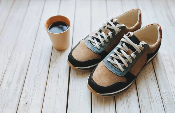 一双羊皮运动鞋放在木制的背景上 还有一杯纸杯咖啡 能量饮料 运动鞋和口渴的概念 — 图库照片