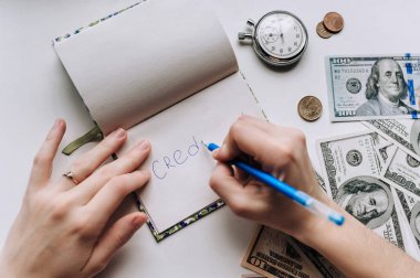 Dişi el, not defterine bir kalem yazar - kredi. Dolar, defter, saat ve kalem. Tefeci, kredi kavramı.