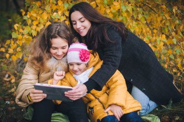 Genç bir anne ve kızları parkta yürürken tabletten ilginç bir şey izliyorlar..