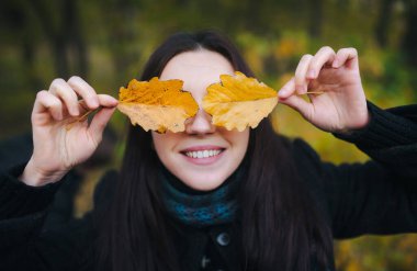 Genç kadın sarı sonbahar yaprakları ile gözlerini kapadı ve neşeyle gülümsedi. Sonbahar parkında yürümek ve sarı sonbahar yapraklarıyla eğlenmek..