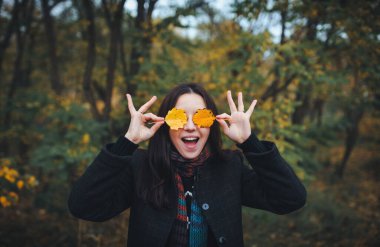 Genç kadın sarı sonbahar yaprakları ile gözlerini kapadı ve neşeyle gülümsedi. Sonbahar parkında yürümek ve sarı sonbahar yapraklarıyla eğlenmek..