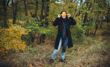 Kız sarı sonbahar yapraklarıyla gözlerini kapatır. Sonbahar ormanında keyifli ve neşeli.