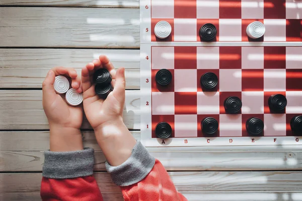The child plays checkers. White and black checkers in children's hands. Children's school of board games.