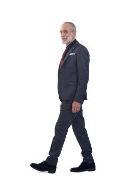 Takım elbiseli, kravatlı beyaz arka planda yürüyen ve kameraya bakan bir adamın yan görüntüsü.