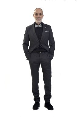 Önde takım elbiseli ve papyonlu bir adam kameraya bakıyor ve iki eli beyaz arka planda.