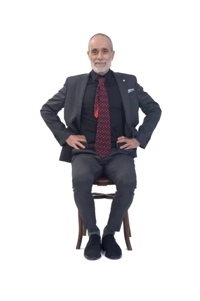 スーツとネクタイと腕のついた椅子に座って白い背景でカメラを見ている男の正面図 — ストック写真