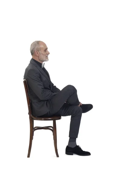 スーツを着た椅子に座って白い背景に足を組んで弓を結ぶ男の側面図 — ストック写真