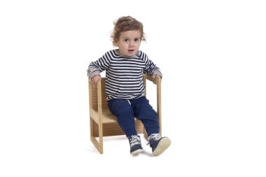 Sandalyede oturan ve beyaz arka plandaki kameraya bakan bir çocuğun ön görüntüsü.