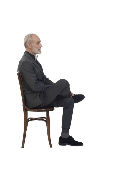 白い背景にスーツと蝶ネクタイの脚を持つ椅子に座っている男の側面図 — ストック写真