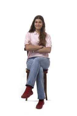 Kollarını kavuşturup beyaz arka planda kameraya bakan, çapraz bacaklı genç bir kızın ön görüntüsü.