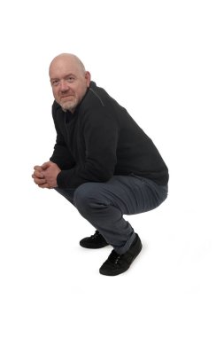 Çömelmiş adam beyaz arka plandaki kameraya bakıyor.