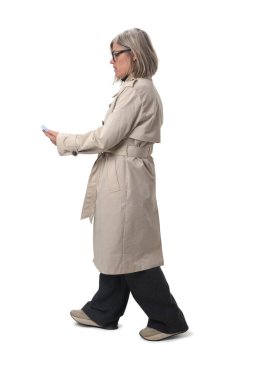 Beyaz arka planda akıllı telefonuna bakan yürüyen kadının yan görüntüsü