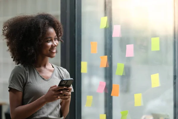 stock image Young African American woman pin weekly planning sticker on the window at home. High quality photo