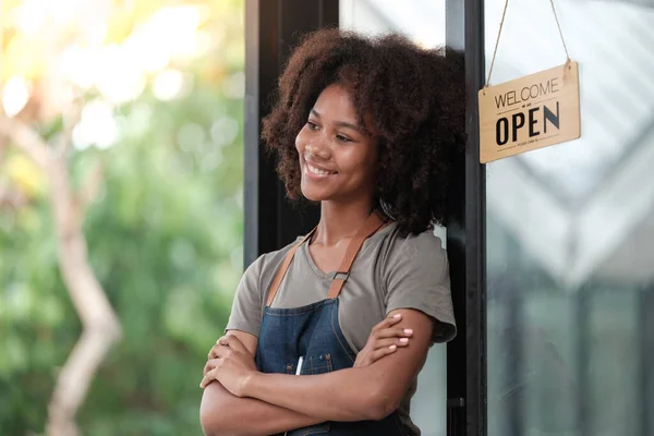 Successful african woman in apron standing coffee shop door. Happy small business owner holding tablet and working. Smiling portrait of SME entrepreneur seller business standing with copy space. High