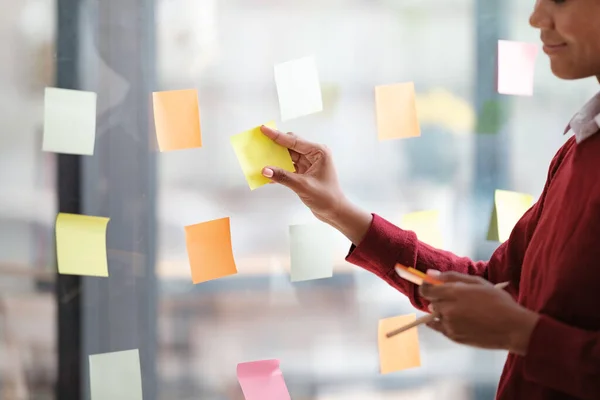 stock image Close up of focused african American female employee write down on colorful sticky notes manage list, concentrated biracial woman work on startup brainstorm collaborate plan on stickers on glass wall