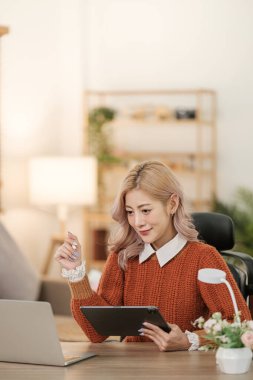 Akıllı telefon bilgisayarı ya da tablet kullanan Asyalı genç bir kadının portresi ev ofisinde çalışıyor, serbest iş dünyası online konsepti. Merhaba Kaliteli Fotoğraf