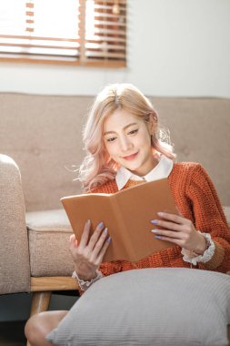Oturma odasında kitap okuyan Asyalı kadının portresi. Sabahları sıcak kahve ya da kakao içiyorum. Yüksek kalite fotoğraf.