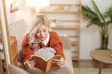 Oturma odasında kitap okuyan Asyalı kadının portresi. Sabahları sıcak kahve ya da kakao içiyorum. Yüksek kalite fotoğraf.