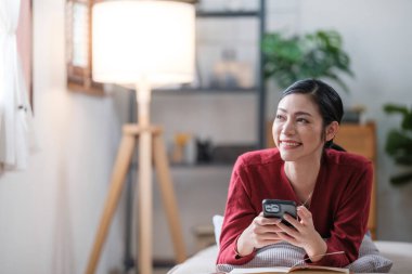 Oturma odasındaki kanepede oturan Asyalı kadın kitap okuyor. Yüksek kalite fotoğraf