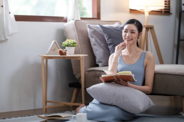 Evdeki kanepede kitap okuyan mutlu genç bir kadın. Yaşam tarzı, serbest çalışma, rahatlama ve oturma odasında kahve içme. Yaşam tarzı kavramı. Yüksek kalite fotoğraf