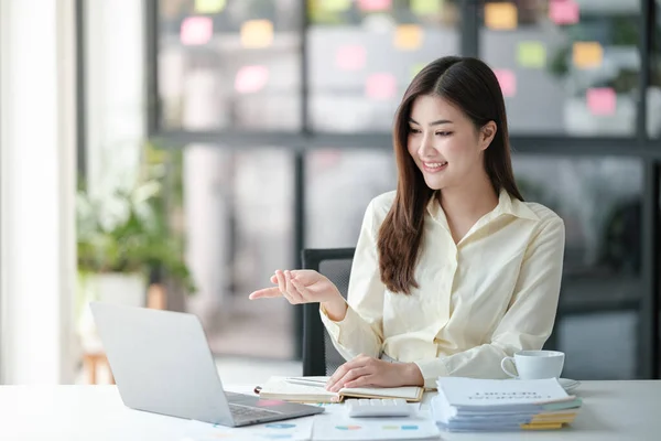 Stock image Photo of attractive woman sitting at desk working on computer looking at screen, smiling, wearing yellow shirt and glasses, typing on keyboard, holding a cup of coffee. High quality photo