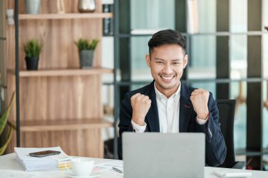 Başarılı ve mutlu Asyalı genç bir adam, iş adamı, mutlu, eliyle evet diyor. Bir anlaşma yaptık. Para kazandım. Modern bir ofiste masada akıllı bir telefon ya da defterle oturmak. Yüksek kalite fotoğraf