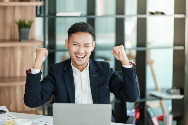 stock image Successful and happy young Asian man, businessman, happy, shows with hand yes. Made a contract. Won money. Sitting with a smart phone or notebook at the table in a modern office. High quality photo