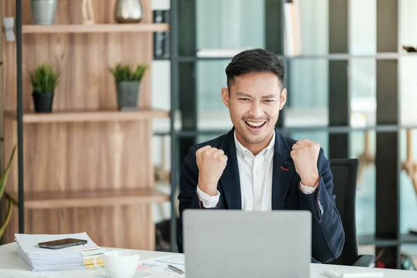 stock image Successful and happy young Asian man, businessman, happy, shows with hand yes. Made a contract. Won money. Sitting with a smart phone or notebook at the table in a modern office. High quality photo