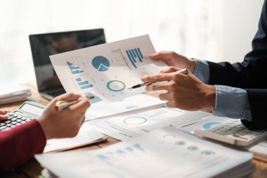 İki Asyalı erkek ve kadın iş adamından oluşan bir ekip ofis masasında dizüstü bilgisayar ve dijital tabletle yeni finansal grafik verilerini tartışıyor. Yüksek kalite fotoğraf