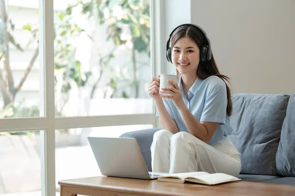 stock image Young woman relaxing and drinking cup of hot coffee or tea using laptop computer on sofa at living room. High quality photo