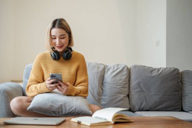 Çekici bir Asyalı kadının portresi akıllı telefon konuşmaları yapıyor evdeki kanepede oturuyor. Yüksek kalite fotoğraf