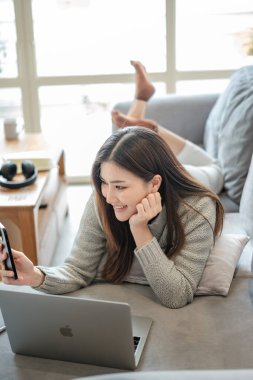 Güzel Asyalı kadın bilgisayarını ve akıllı telefonunu iletişim kurmak için kullanır, evde mutlu bir şekilde çalışır, serbest çalışanlar evdeki özel odalarda çalışır ya da çevrimiçi iletişimde öğrenirler. Merhaba Kaliteli Fotoğraf.