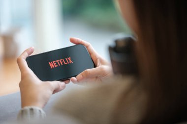 CHIANG MAI, THAILAND - 23 Haziran 2023: Bir kadın Netflix eğlence platformlu elmalı iPhone 14 'ü evinde tutuyor. Yüksek kalite fotoğraf