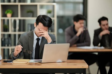 İş adamları ofisinde dizüstü bilgisayarlarıyla oturup, kendilerini baskı altında ve yorgun hissediyorlar. Yüksek kalite fotoğraf
