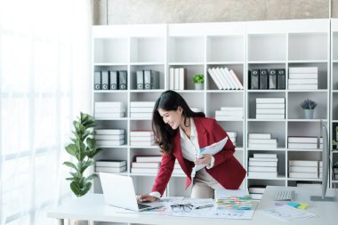 Güzel Asyalı iş kadını dizüstü bilgisayar üzerinde çalışıyor ve istatistik veri grafikleri ve grafiklerinden finansal hesap makinesi ile hesap yapıyor. Modern ofiste başarılı iş sonuçları kırmızı gömlek giyer. Yüksek kalite