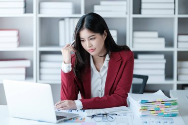 Güzel Asyalı iş kadınının dizüstü bilgisayarla çalışıp istatistik veri grafikleri ve grafiklerinden finansal hesap makinesiyle hesap yaptığını düşünüyor. Modern ofis kırmızı gömlek giyer. Yüksek kalite fotoğraf