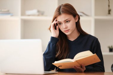 Düşünüyorum da, güzel beyaz bir kız öğrenci uzaktan çalışıyor. Evde dizüstü bilgisayar ve not defteriyle bir masada oturuyor ve bir video konferansı izliyor. Yüksek kalite fotoğraf
